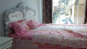 A bedroom with a white bed, pink floral bedding, and a view of the outside through a window. - Just Inn Semarang (Semarang)