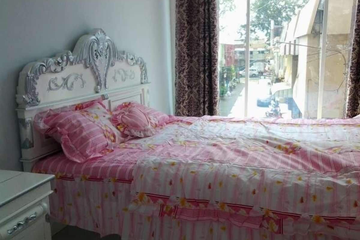 A bedroom with a white bed, pink floral bedding, and a view of the outside through a window.