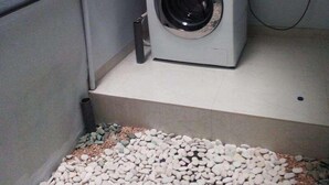 A compact laundry room with a front-loading washing machine, a small shelf, and a pebble-filled area. - Just Inn Semarang (Semarang)