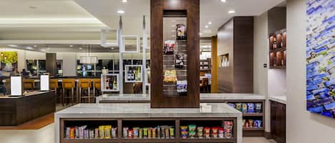 A modern food court with a central serving area, multiple seating options, and a variety of food and drink products on display.