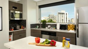 A modern kitchen with a large window, stainless steel appliances, and a variety of fresh produce on the counter.