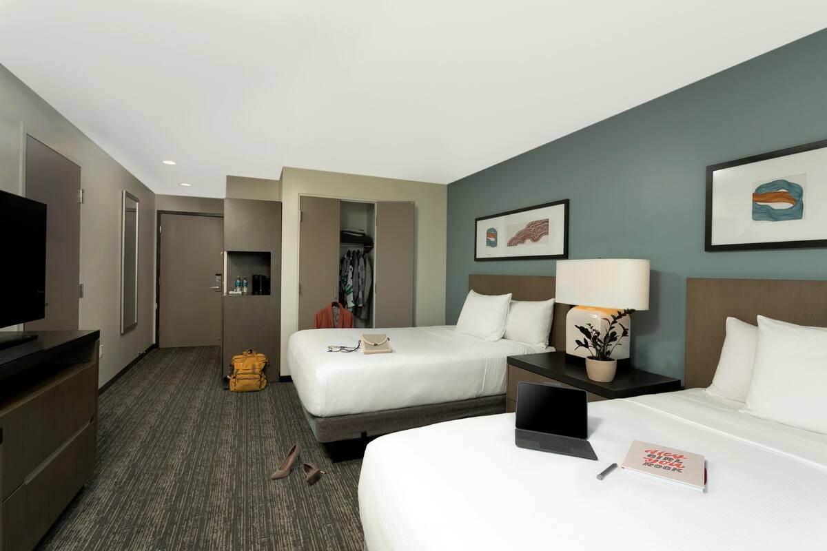 Een hotelkamer met twee bedden, een bureau met een laptop, een televisie en een kledingkast.