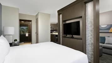 A hotel room with a large bed, a TV, a sofa, a desk, and a bathroom visible through an open door.