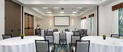 A conference room with round tables, chairs, a projector screen, and a carpeted floor.