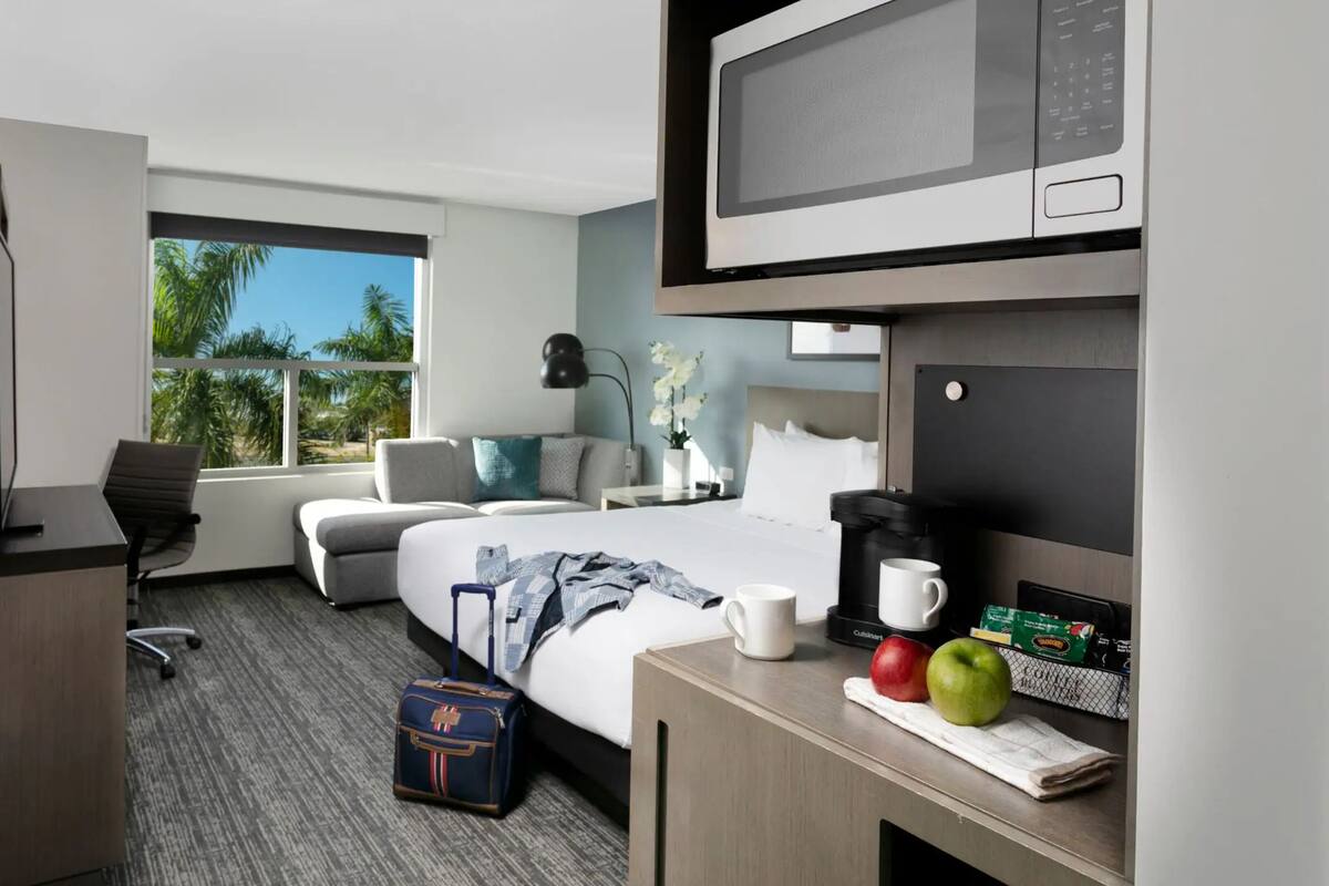 Een hotelkamer met een bed, een bureau met koffiezetapparaat, een koffer en een televisie.
