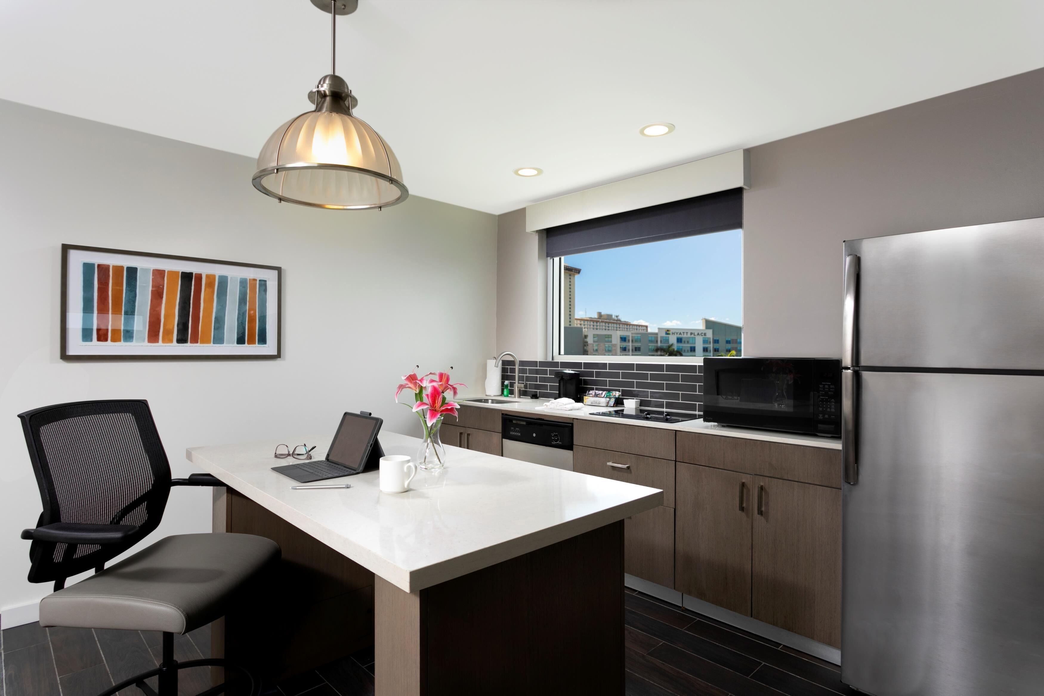 A modern kitchen with a large island, stainless steel appliances, and a view of buildings through a window.