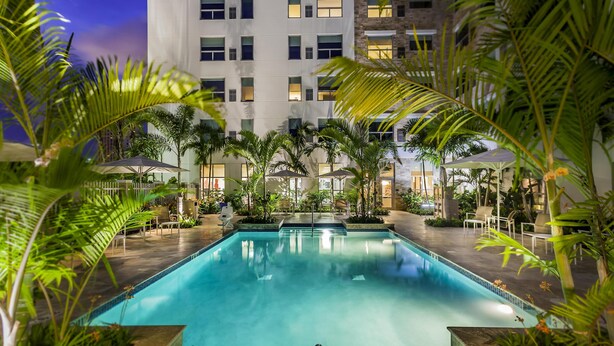 A swimming pool surrounded by palm trees and a building with multiple windows.