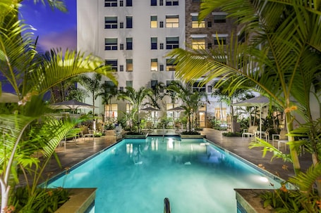 A swimming pool surrounded by palm trees and a building with multiple windows.