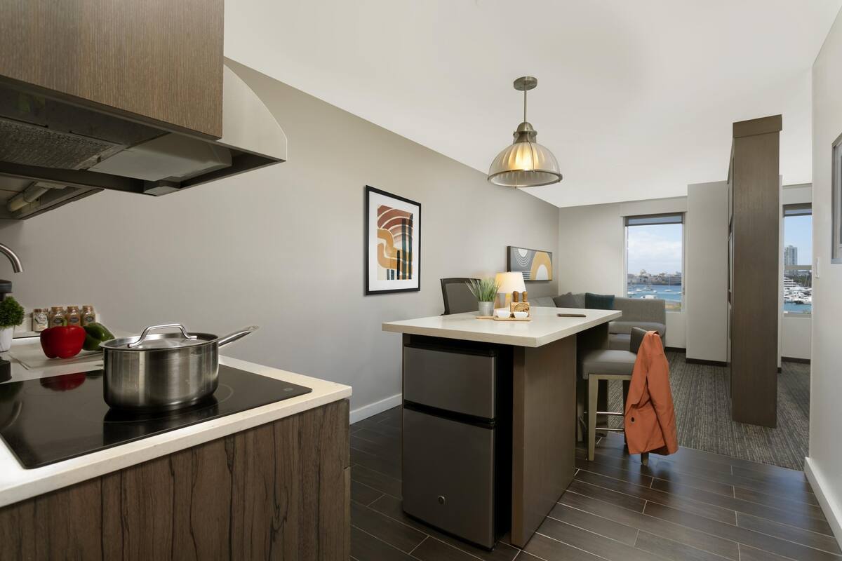 Een moderne keuken met een inbouwfornuis, een kleine koelkast en een eethoek met een bank en een hanglamp.