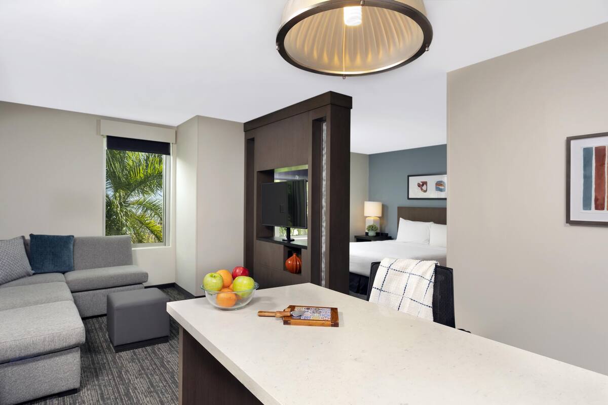 Een hotelkamer met een bank, een eettafel met fruit, een televisie en een bed.
