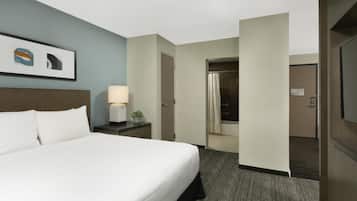 Une chambre d’hôtel avec un lit, une table de chevet avec une lampe, un tableau encadré et une porte de salle de bain.