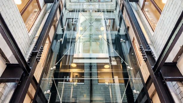 Un atrio a più livelli con ringhiere in vetro, un'asta centrale per l'ascensore e un design architettonico moderno.