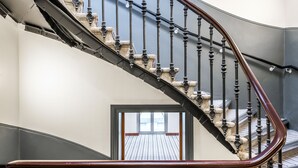 Una scala a chiocciola con ringhiera in metallo lucido e balaustre nere, che conduce a una zona d'appoggio con vista su un balcone.