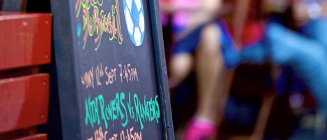A chalkboard with event details, a red bench, and a blurred background of people.