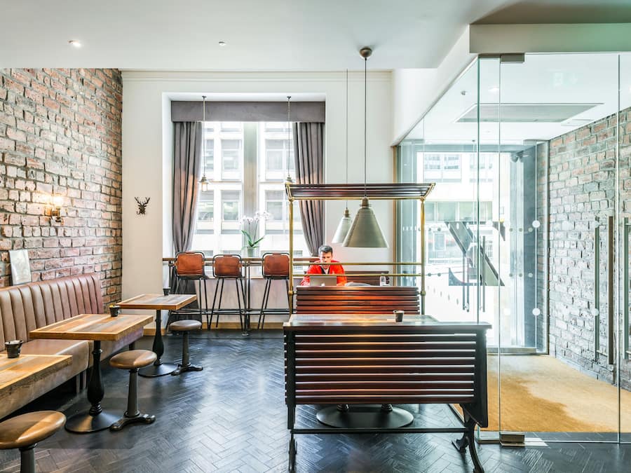 A modern interior with a brick wall, wooden furniture, and large windows offering views of the city.