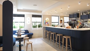 A modern bar area with a counter, stools, and a seating area with sofas and tables. - The Z Hotel Piccadilly (London)