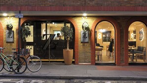 A brick building with numbered doors, a reception area, and a seating area visible through the windows. - The Z Hotel Piccadilly (London)