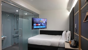 A hotel room with a bed, a TV mounted on the wall, a glass shower enclosure, and a wooden wardrobe. - The Z Hotel Piccadilly (London)