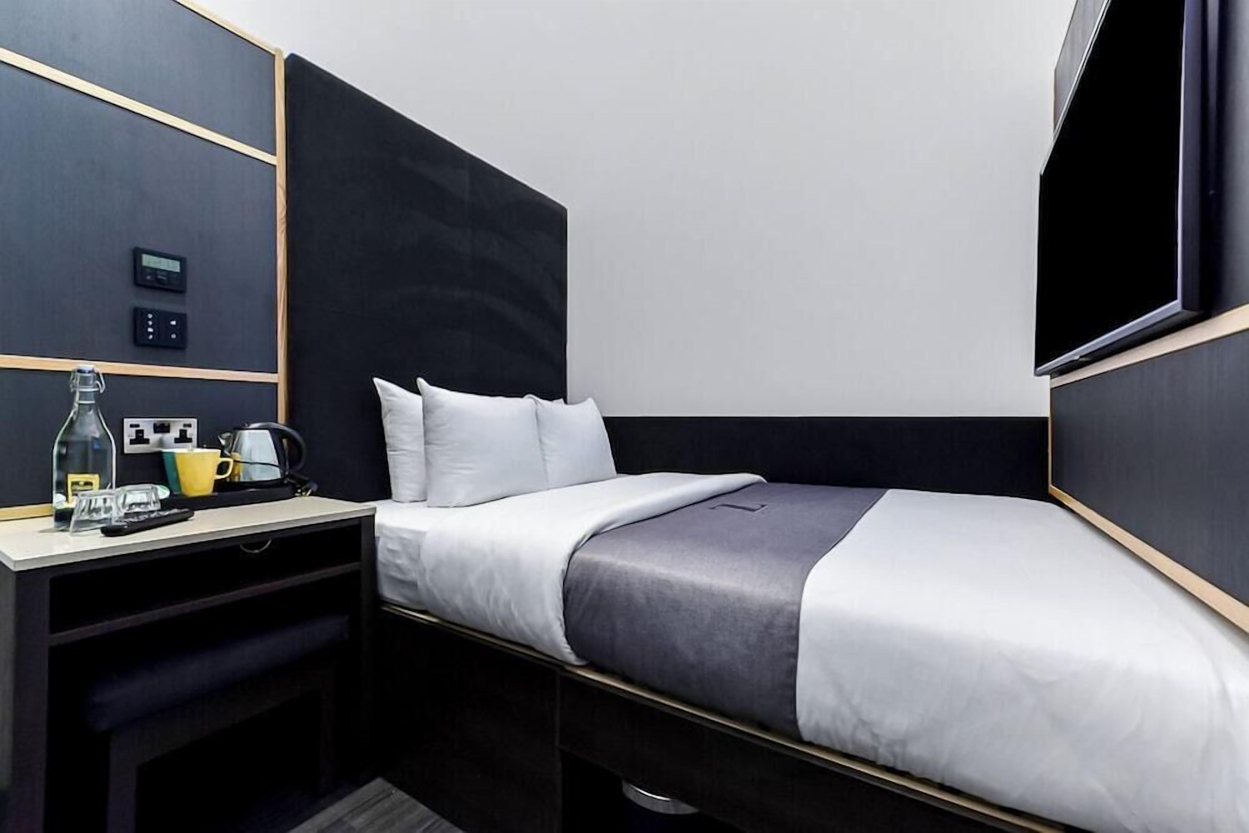 A compact hotel room with a bed, bedside table, and a flat-screen TV.