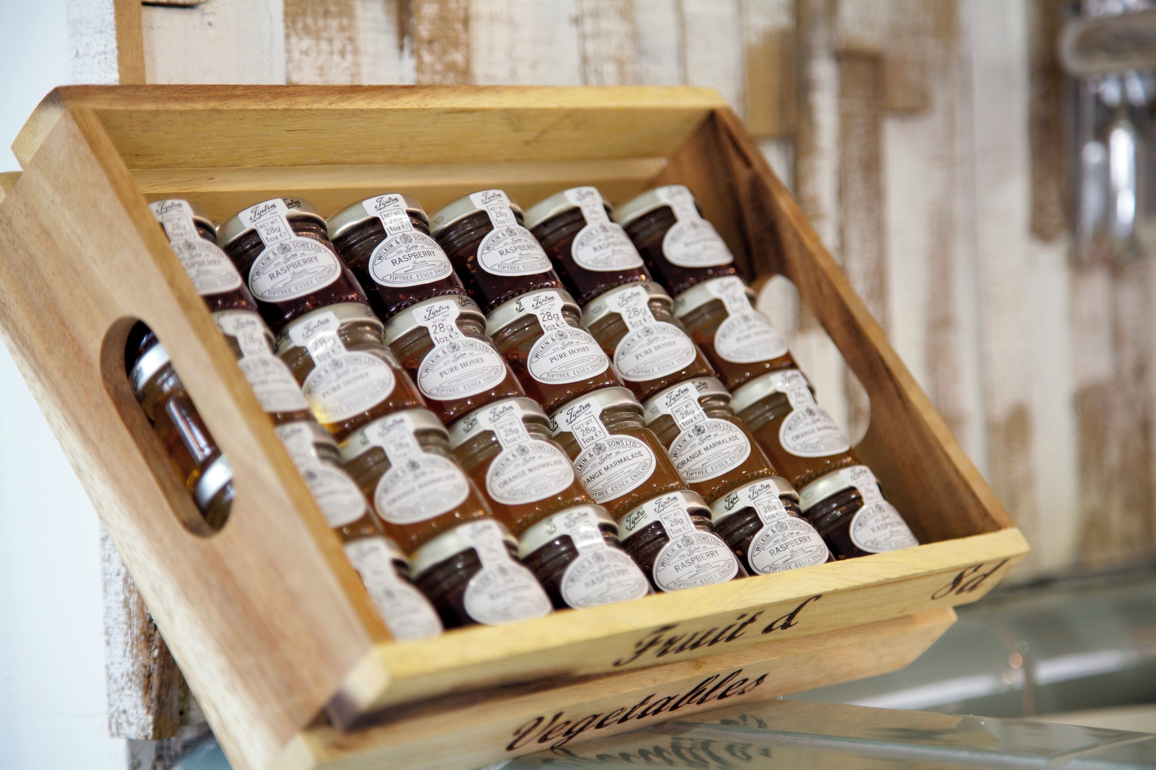 A wooden crate filled with jars of preserves, labeled with various flavors like raspberry and orange marmalade.