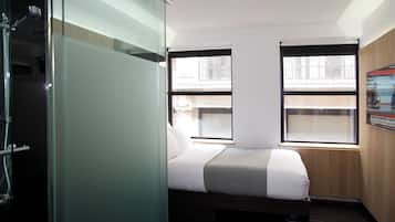 Una habitación de hotel moderna con cama, ducha y dos ventanas que ofrecen vistas a la ciudad.