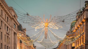 A person standing on a sidewalk holding an umbrella, with a street decorated with lights and a car passing by. - The Z Hotel Piccadilly (London)