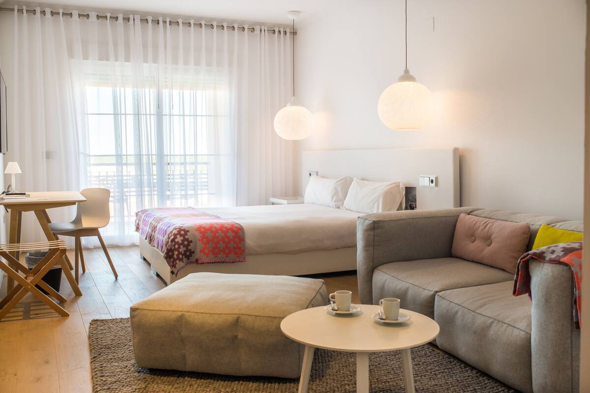 Una habitación de hotel moderna con cama, sofá, una pequeña mesa con tazas, escritorio y silla.
