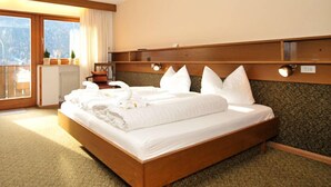 A hotel room with a wooden bed, a view of the outdoors through a large window, and a wooden headboard with wall-mounted lights. - Raschötzhof (Funes)