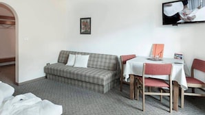 A hotel room with a sofa, a dining table with chairs, a TV mounted on the wall, and a framed picture on the wall. - Raschötzhof (Funes)