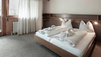 Habitación de hotel con una cama grande, cabecera de madera, radiador y vistas al exterior a través de una ventana con cortinas.