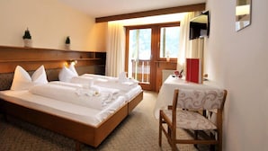 A hotel room with a large bed, a small table with a chair, and a window with curtains. - Raschötzhof (Funes)