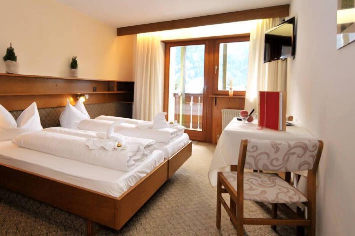 A hotel room with a large bed, a small table with a chair, and a window with curtains.