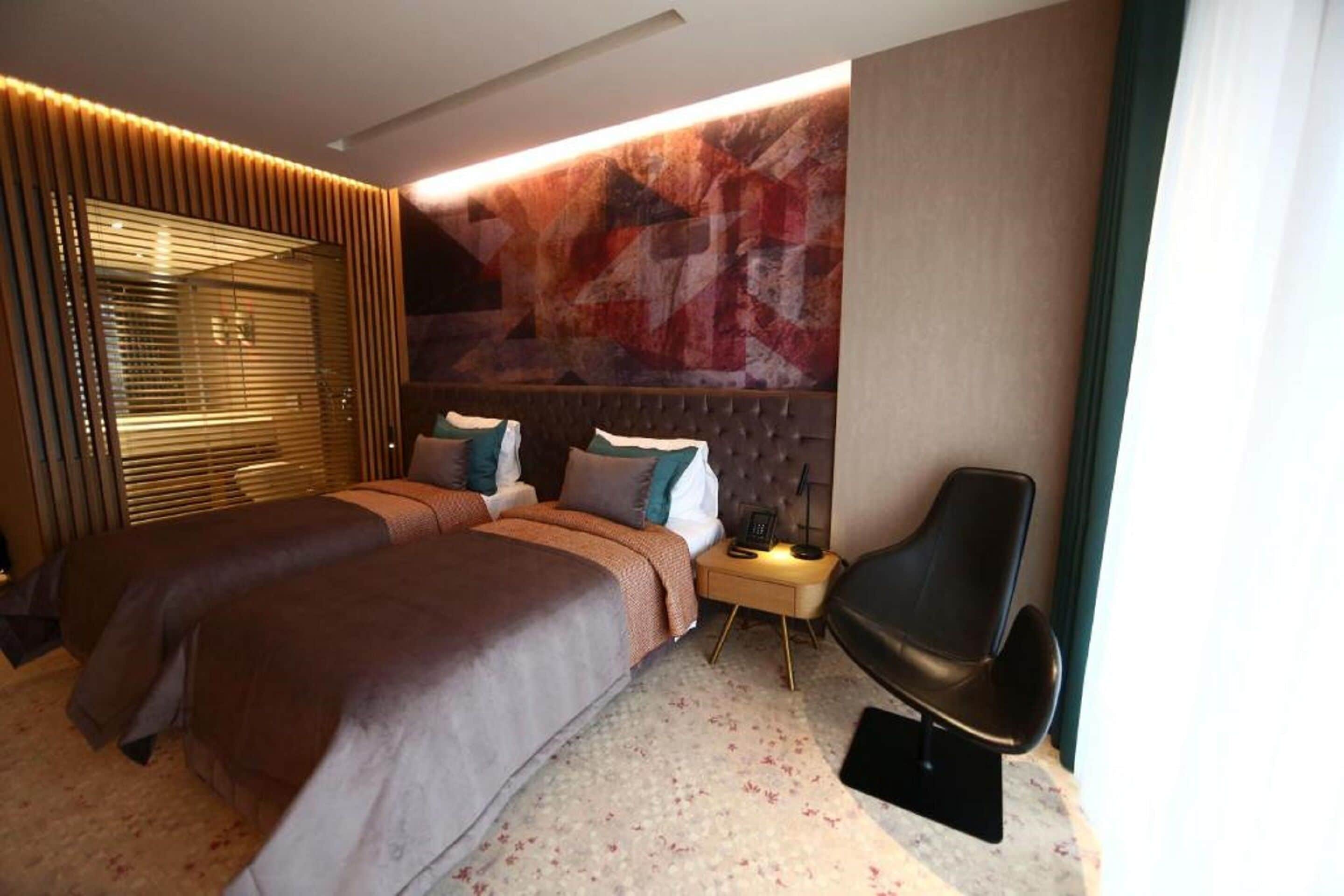 A modern hotel room with a large bed, a bedside table with a lamp, and a decorative wall.