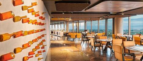 Un restaurante moderno con una larga pared de botellas vacías, amplias ventanas y un suelo pulido.