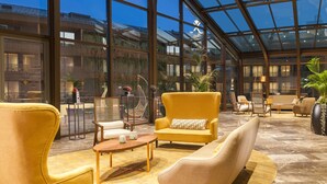 A spacious indoor area with large windows, yellow upholstered chairs, and a variety of seating options.