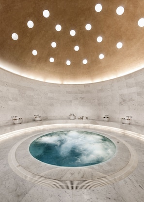 A modern spa with a central hot tub, marble walls, and a ceiling with circular lights.