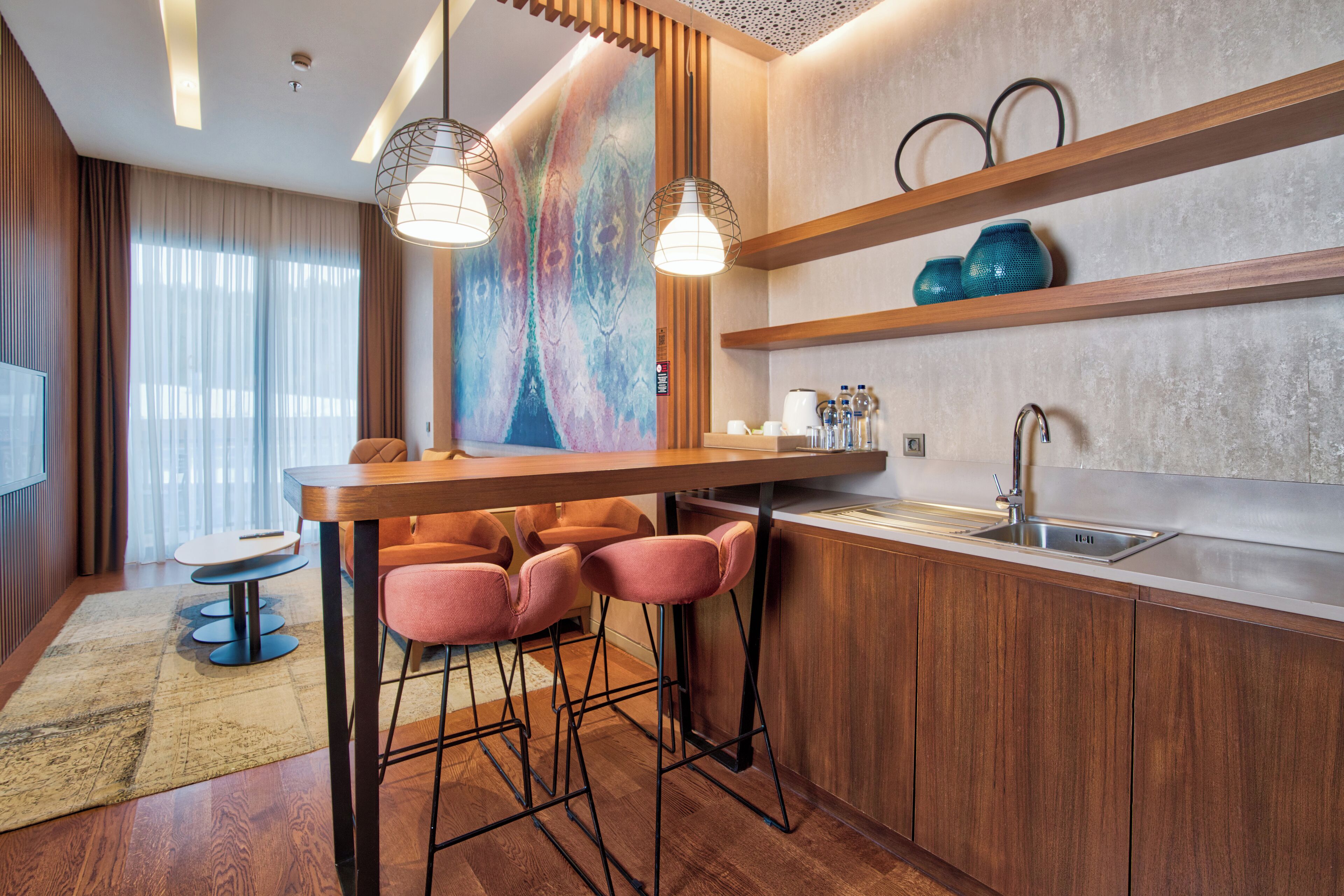 A modern kitchen with a bar area, wooden cabinets, and a colorful abstract wall.