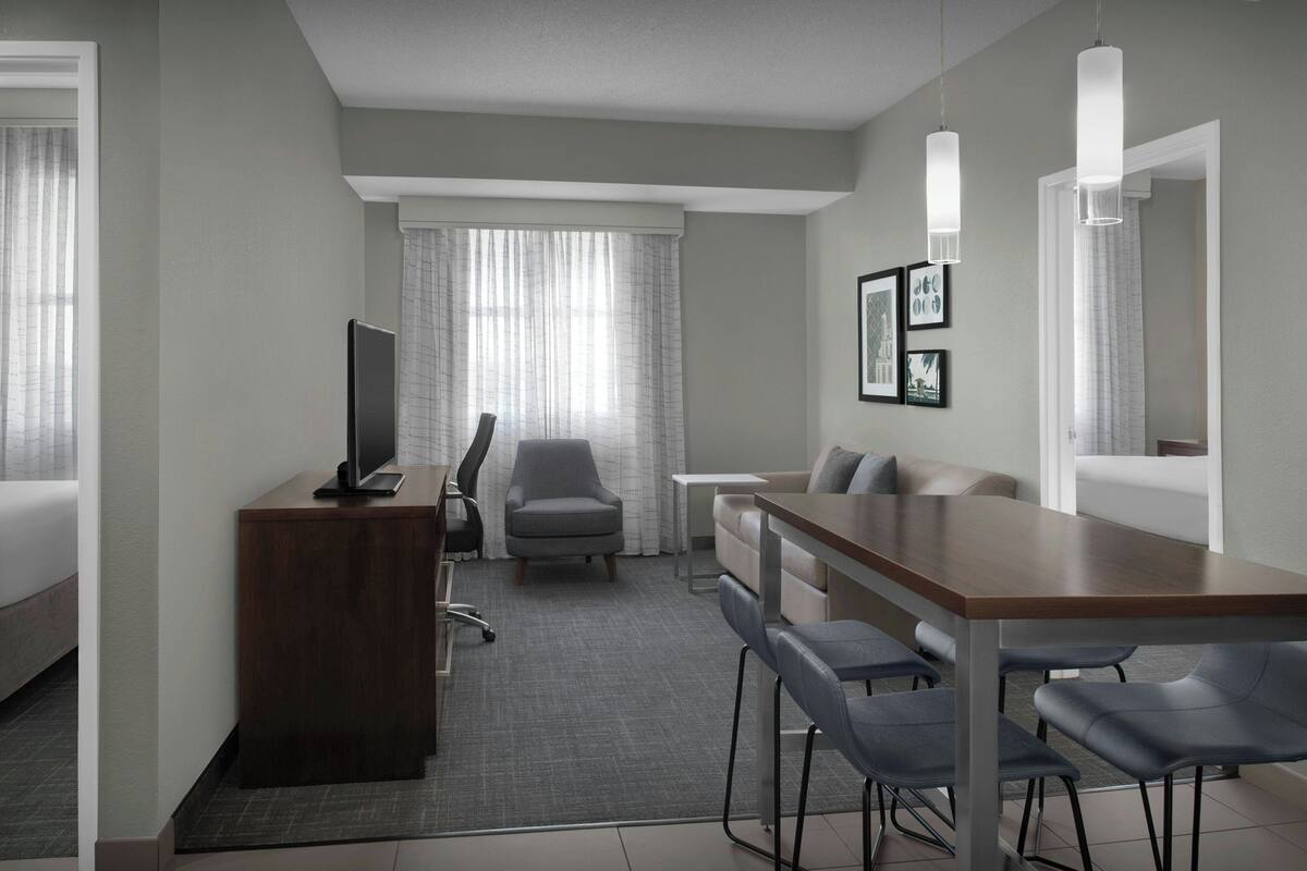 A hotel room with a bed, a desk with a chair, a sofa, a TV, and a dining table with chairs.