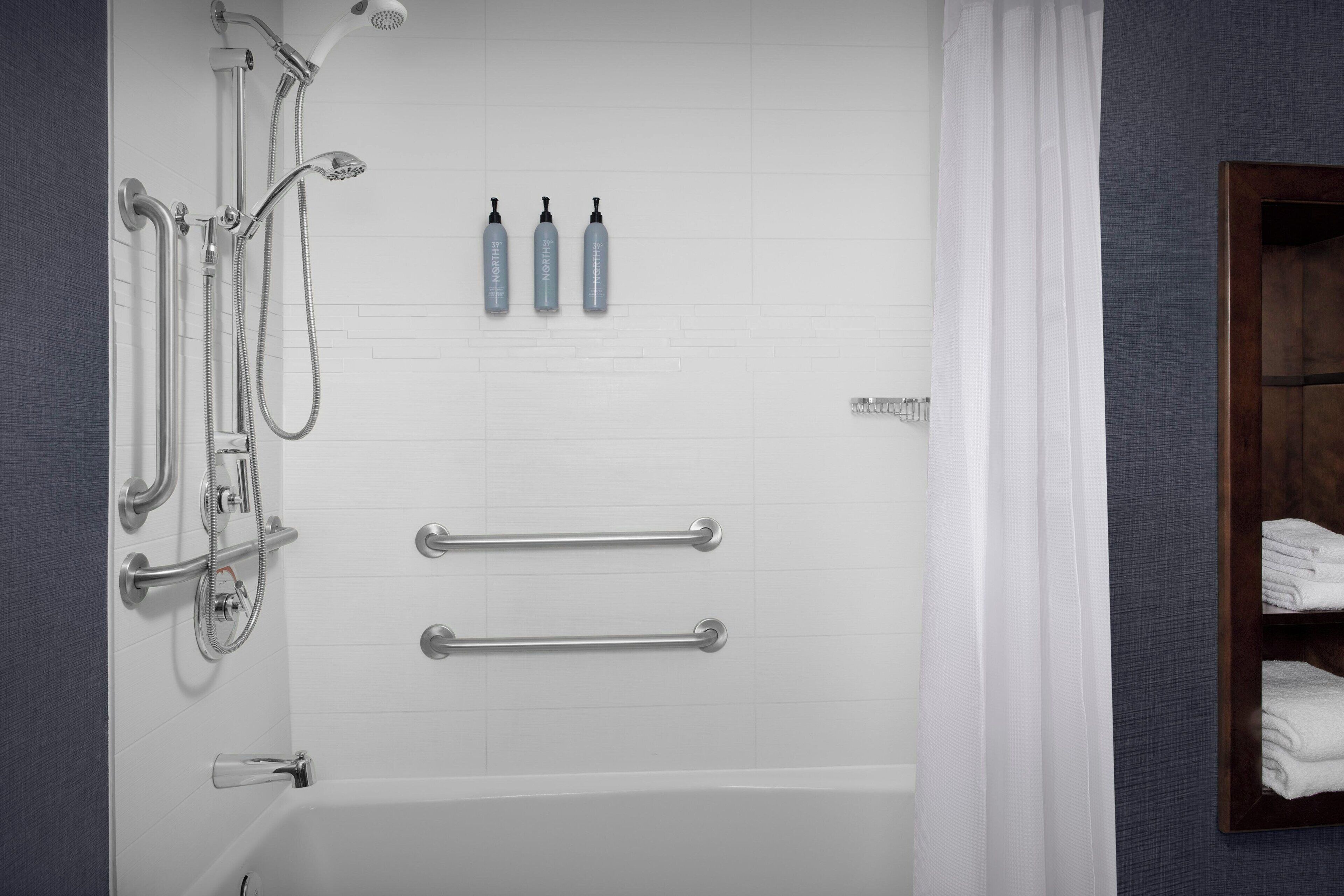 A modern bathroom with a bathtub, shower, and handrails.