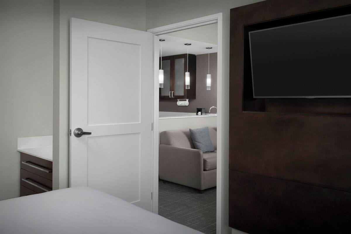 A hotel room with a bed, a bathroom with a mirror, a sink, and a TV on the wall.