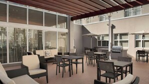 Un espacio al aire libre con mobiliario de mimbre, una parrilla y ventanas amplias.