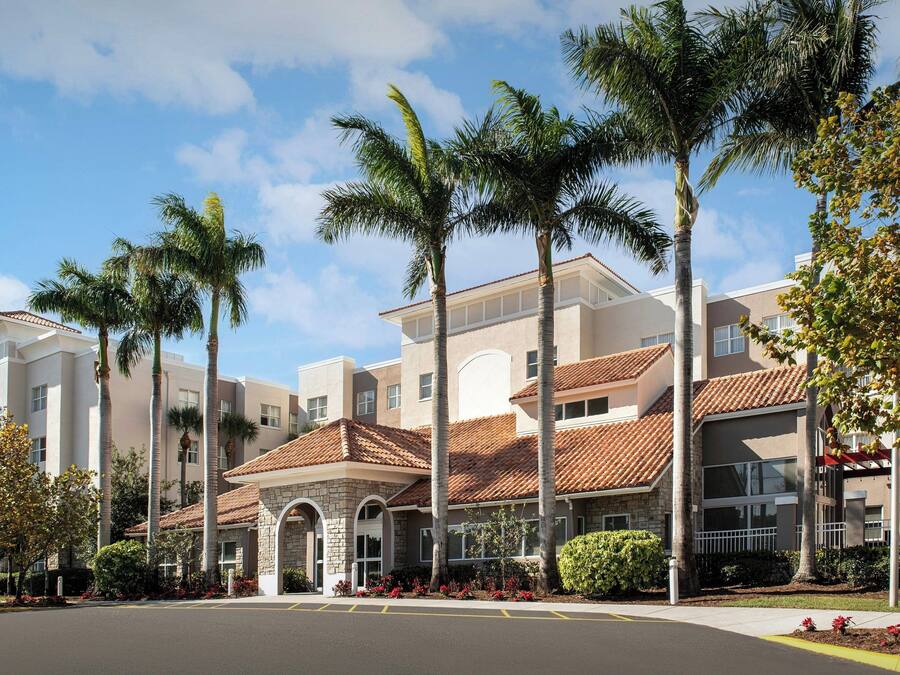 A multi-story hotel with a central courtyard, palm trees, and a tiled roof.