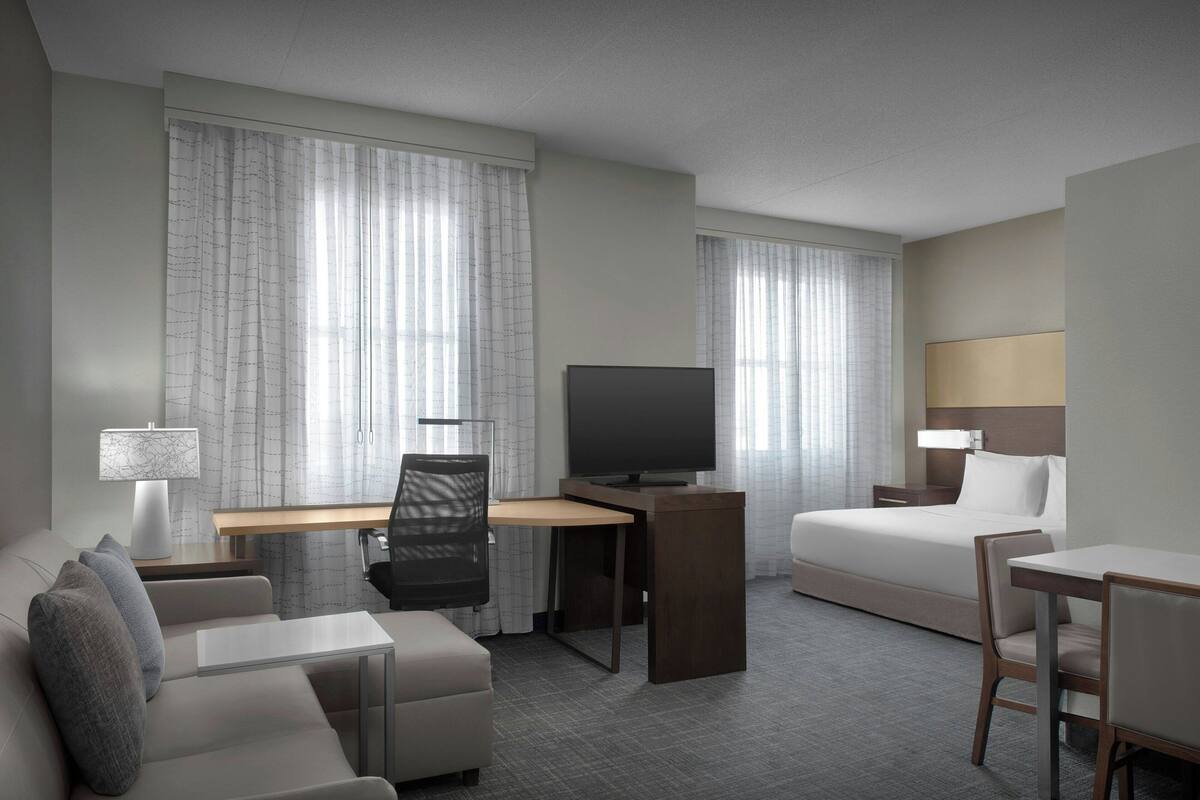 A hotel room with a bed, a desk with a TV, a sofa, and a chair.