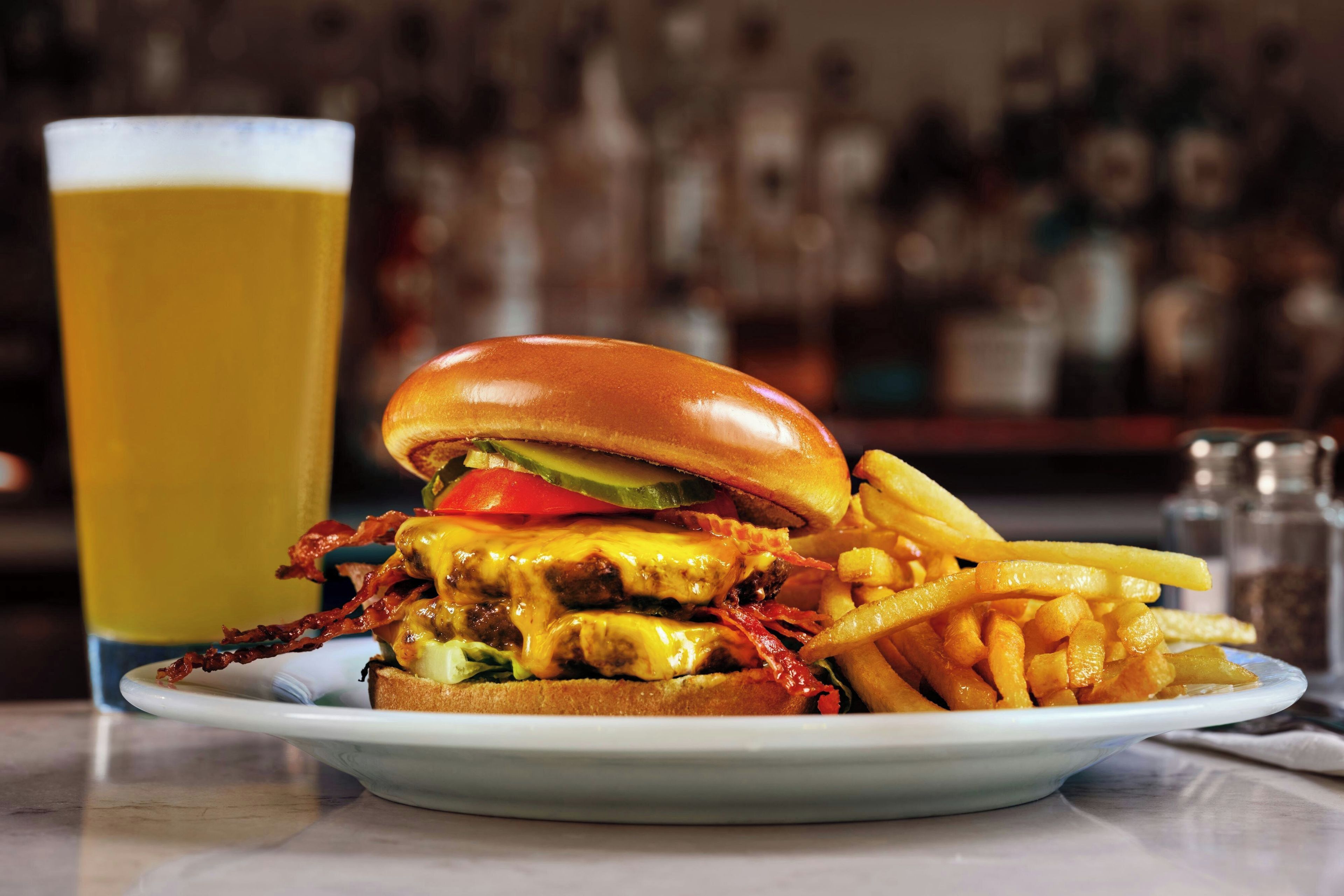 Un plato con una hamburguesa, papas fritas y una jarra de cerveza.