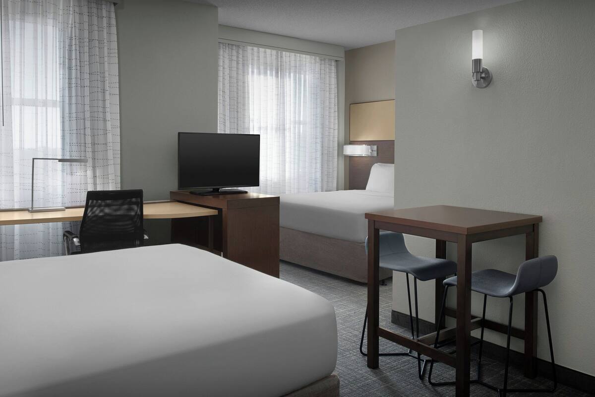 A hotel room with a bed, a desk with a chair, a television, and a small table with two chairs.