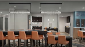 Un comedor moderno con una mesa larga y sillas anaranjadas, una cocina al fondo e iluminación colgante.
