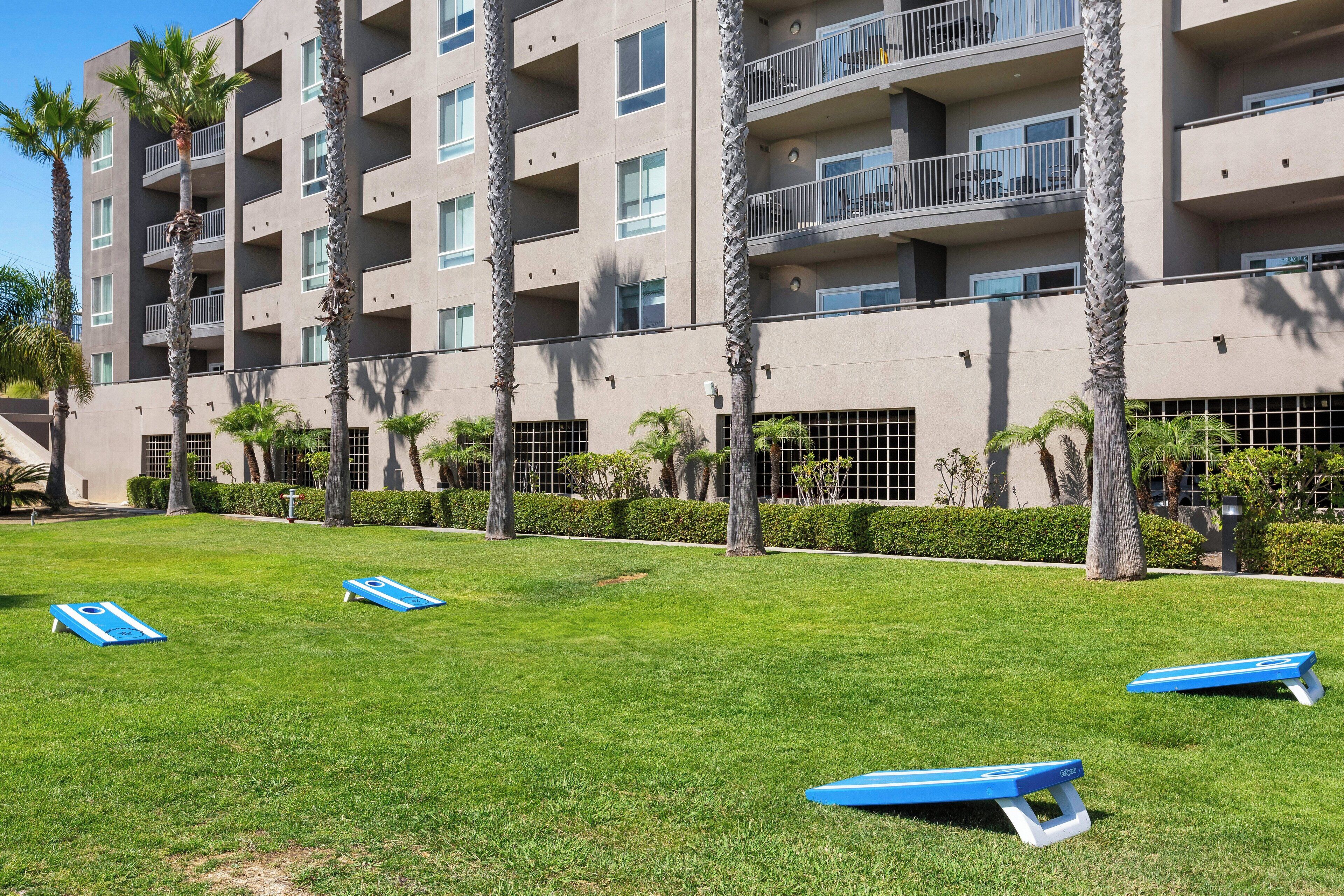 A multi-story hotel with balconies, palm trees, and a well-maintained lawn with shuffleboard tables.