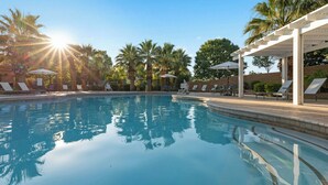 A swimming pool with sun reflecting on the water, surrounded by lounge chairs and umbrellas. - WorldMark St. George (St. George)