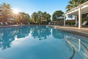 A swimming pool with sun reflecting on the water, surrounded by lounge chairs and umbrellas.