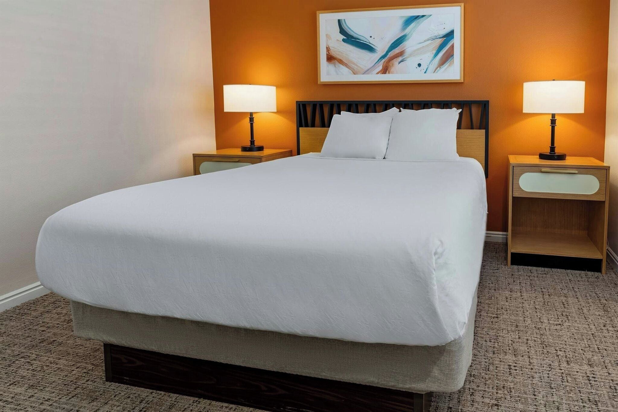 A hotel room with a large bed, two bedside tables with lamps, a headboard, and a painting on the wall.